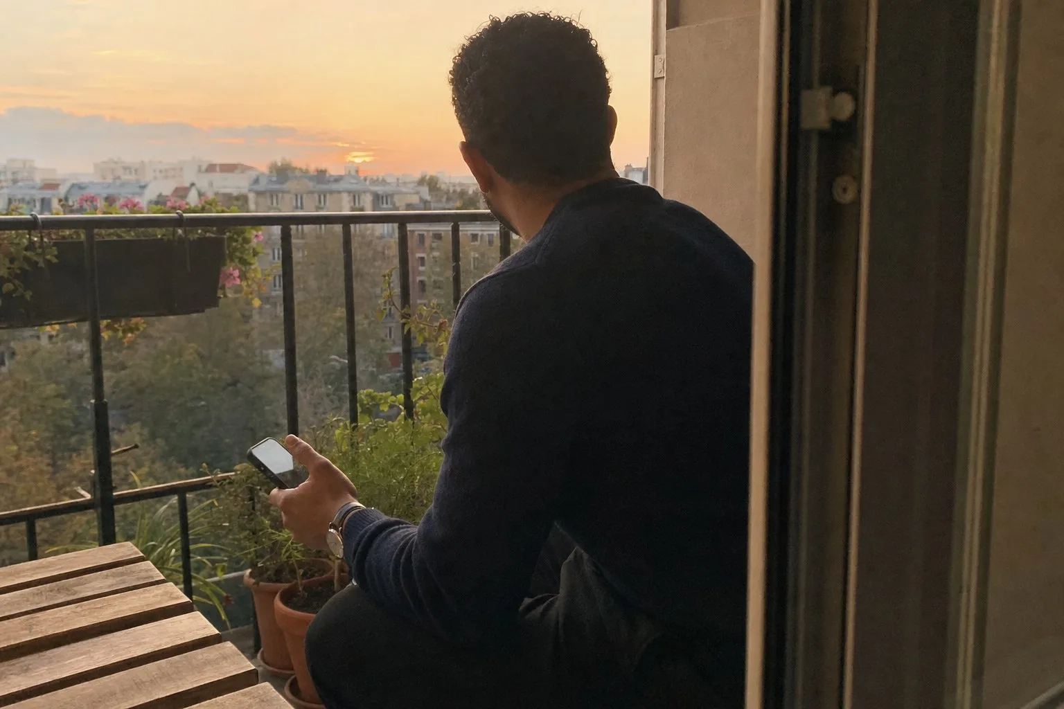 A man on a balcony at sunset, relaxed, holding his phone