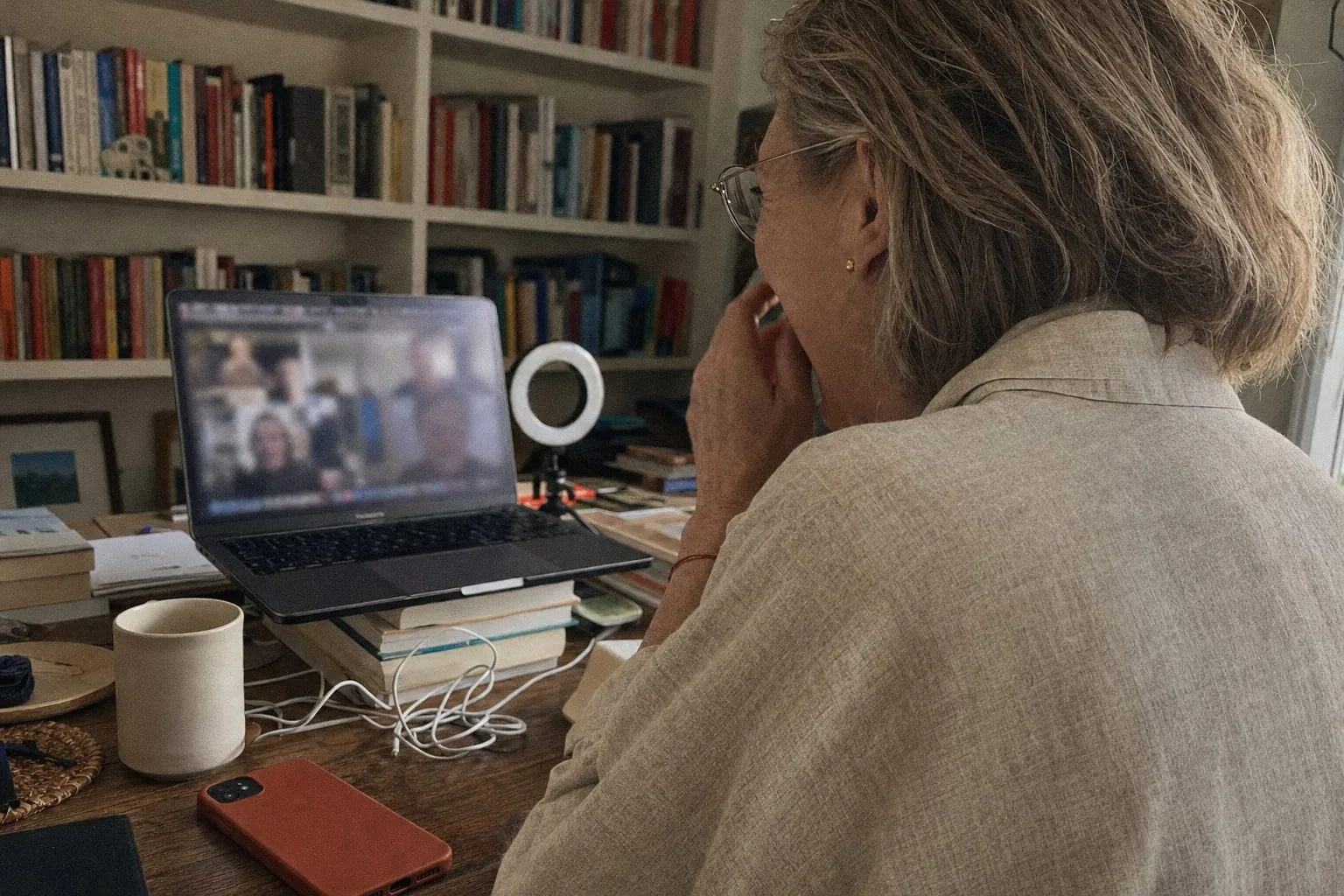 A woman at a home desk laughing during a video call, seen from behind