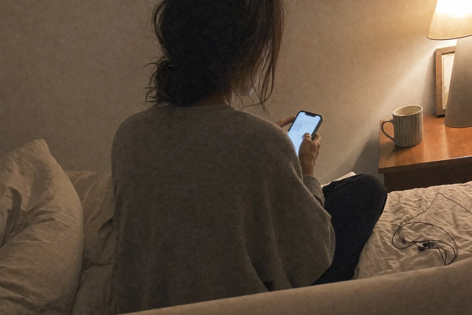 Someone sitting cross-legged on a bed late at night, phone glowing in both hands