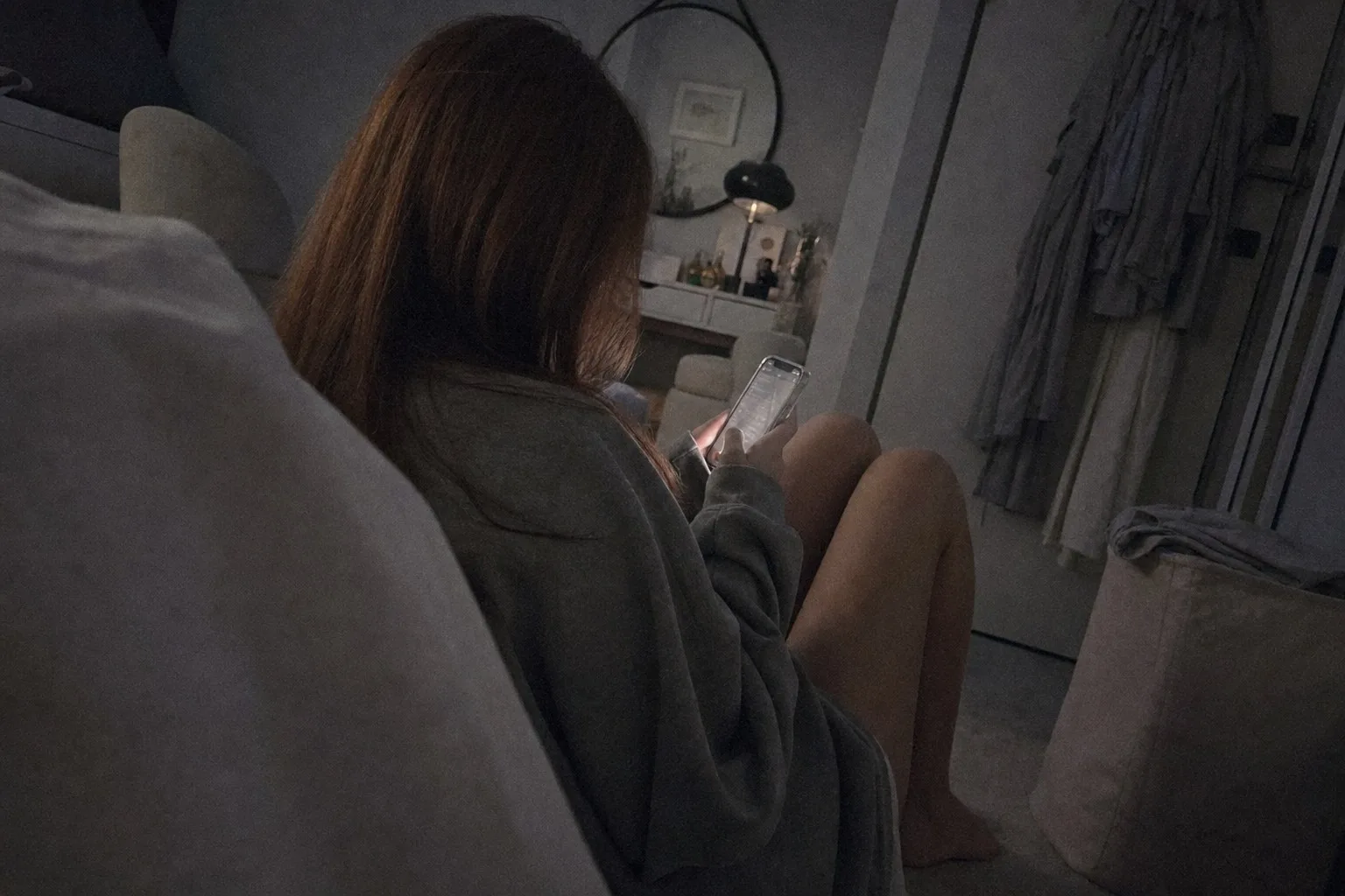 A person sitting on her bedroom floor at night reading news on her phone